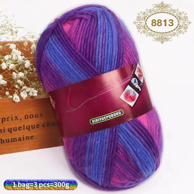 A skein of gradient dyed purple and blue wool blend yarn with a brown label and a gold stamp.