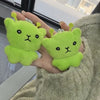 A pair of soft, lime green alien plush keychains are held in a person's hand against a blurred background.