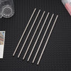 A set of six slender stainless steel straws laid diagonally on a dark surface.