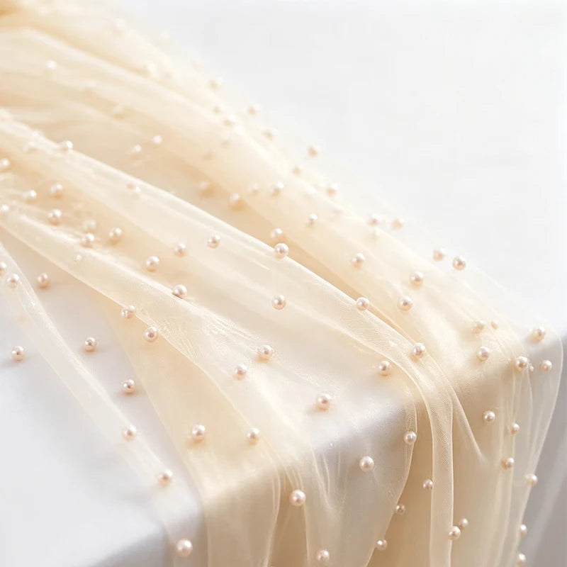 Elegant faux pearl tulle table runner in beige fabric draped on a white surface.