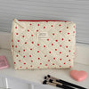 A cream-colored quilted makeup bag with a red heart pattern resting on a white surface.