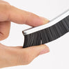 A hand holds a black grout cleaning brush set with hard bristles.