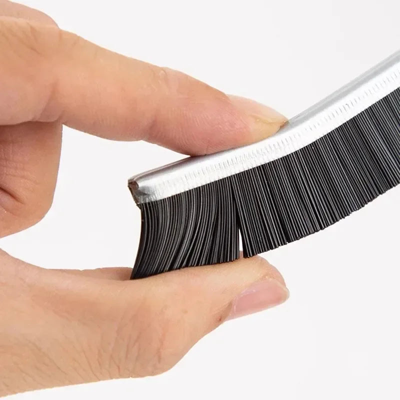 A hand holds a black grout cleaning brush set with hard bristles.