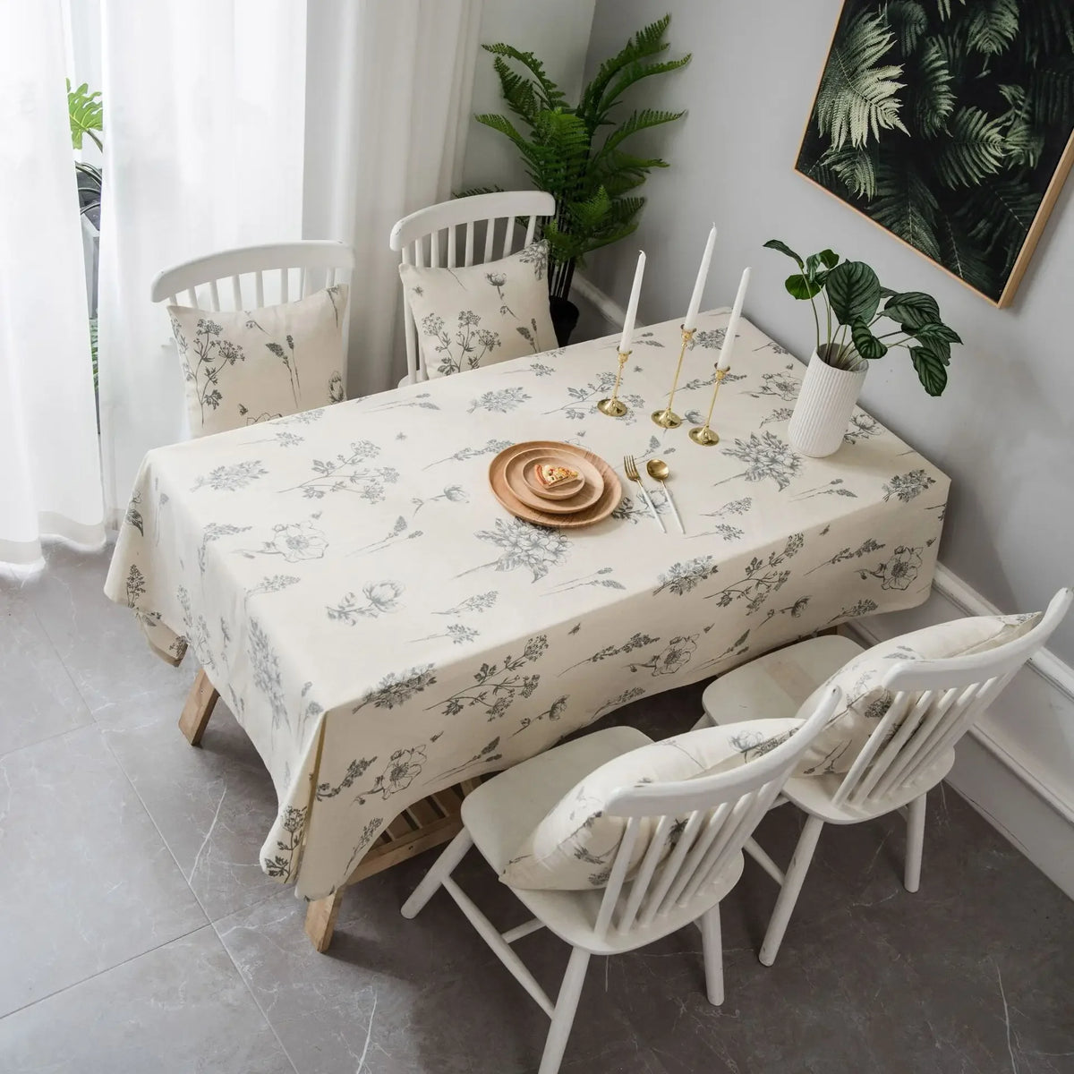 A dining table set with a cream tablecloth featuring a rustic fern print, surrounded by white wooden chairs.
