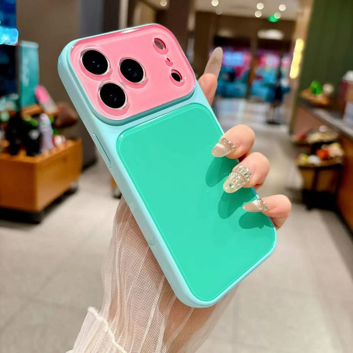 A hand holds a color blocking shockproof phone case with a pink and teal design.