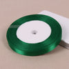 A roll of emerald green lustrous satin ribbon with a white center, placed on a light beige surface.