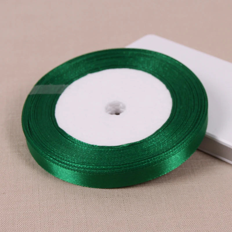 A roll of emerald green lustrous satin ribbon with a white center, placed on a light beige surface.