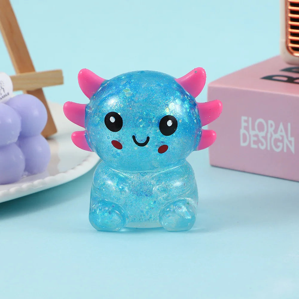 A bright blue squishy stress ball shaped like an axolotl with pink accents, resting on a light blue surface.