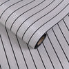 Roll of 3D grille pattern peel-and-stick wallpaper with vertical black lines on a light gray background