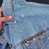 Nahaufnahme von blauem Jeansstoff mit silbernen Stern-Nieten und goldenen Kettendetails