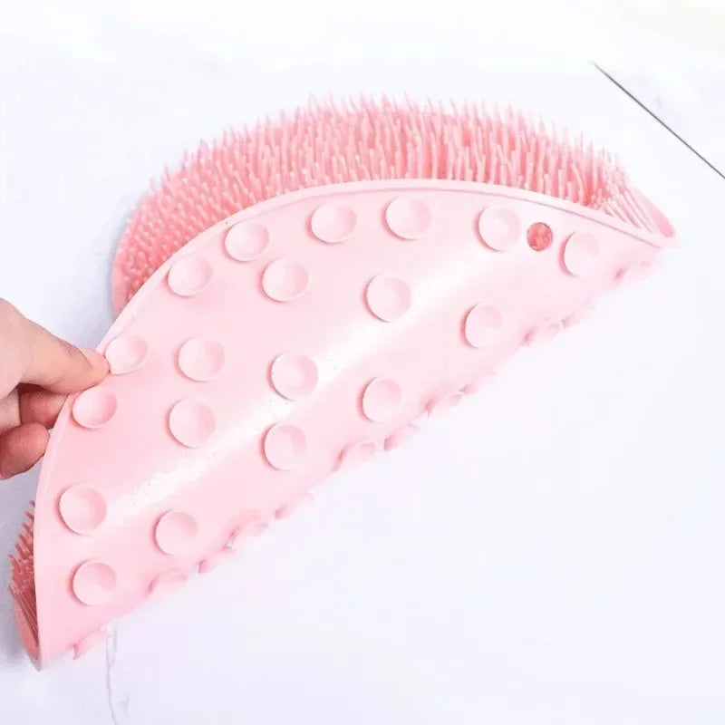 A pink non-slip silicone shower mat with exfoliating bristles is shown being held by a hand.