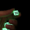 A hand holds glowing green acrylic dice, illuminating a dark background.