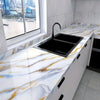 A kitchen countertop with a black sink and white marble featuring gold veining, set in a modern home interior.