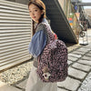 A young woman wearing a pink leopard print nylon backpack and a white skirt stands outdoors near a metal structure.