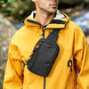A man wearing a yellow jacket with a black hood and a black sling bag attached to the chest.