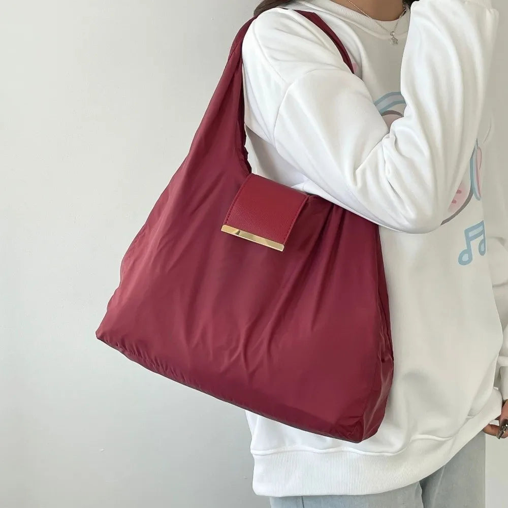 A maroon retractable keychain tote bag with a gold accent folds into a compact pouch, carried by a person wearing a white swe