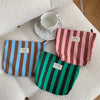 A collection of striped canvas cosmetic bags in blue, pink, and green resting on a white surface with a ceramic cup.