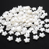 A pile of 100 white acrylic pearl spacer beads for jewelry making scattered on a dark surface.