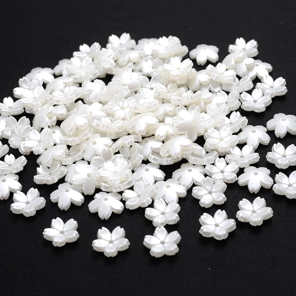 A pile of 100 white acrylic pearl spacer beads for jewelry making scattered on a dark surface.