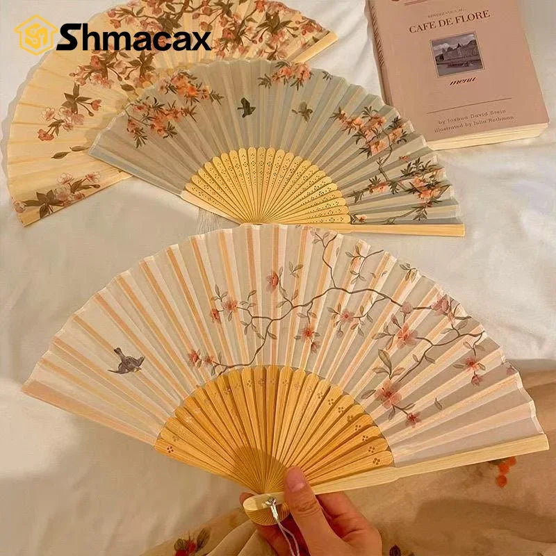 A light wood folding fan with a floral design is displayed on a white surface.