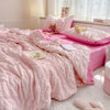 A pink breathable summer seersucker quilt spread on a bed with a pink pillow and a stuffed animal.