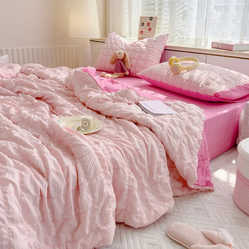 A pink breathable summer seersucker quilt spread on a bed with a pink pillow and a stuffed animal.