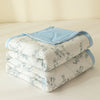 A stack of light blue and white quilted blankets or quilts on a bed.
