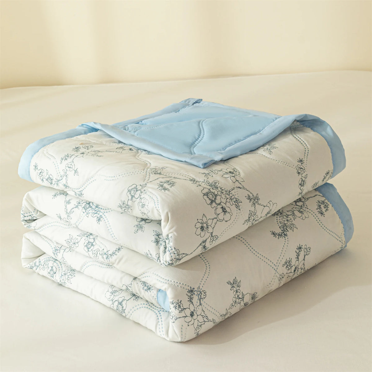 A stack of light blue and white quilted blankets or quilts on a bed.