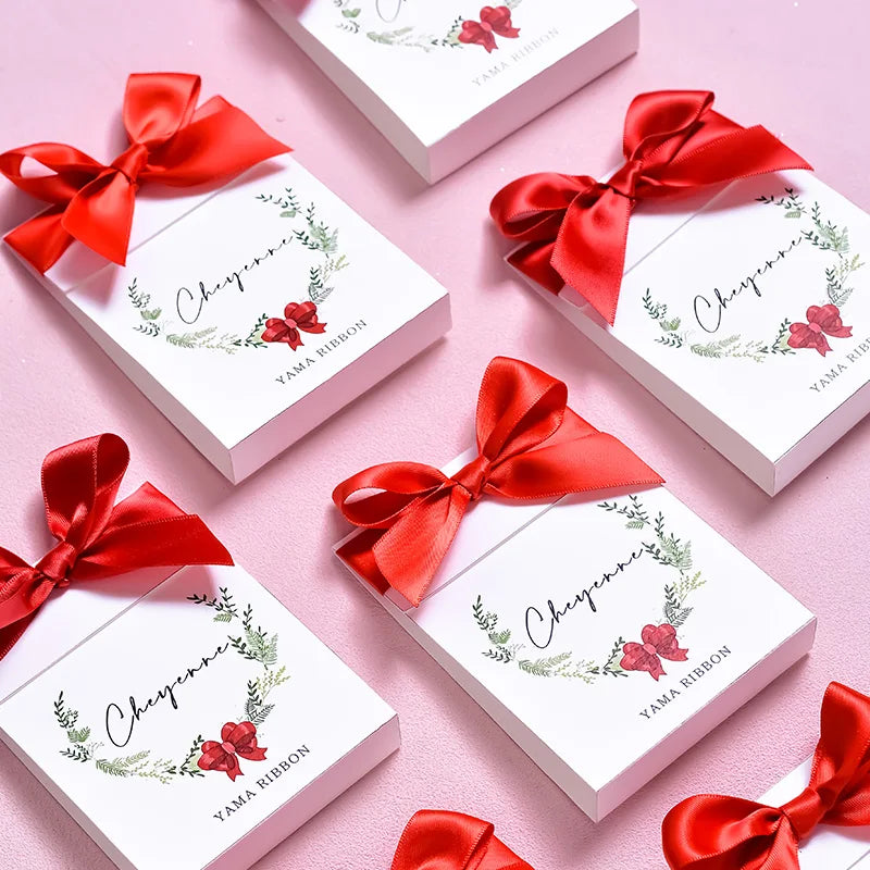 A collection of elegant red satin ribbon rolls tied in bows, displayed on white gift boxes.