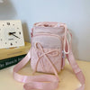 A pink bow-decorated casual crossbody bag with an adjustable strap resting on a light surface.