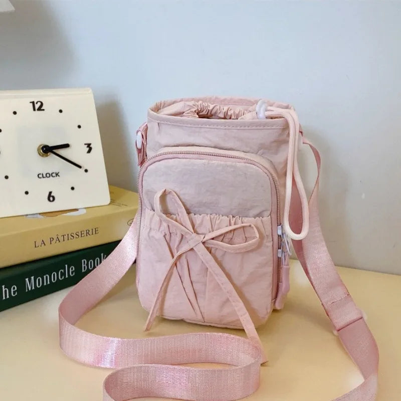A pink bow-decorated casual crossbody bag with an adjustable strap resting on a light surface.