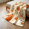 A cozy flannel throw blanket featuring an autumn design with pumpkins and maple leaves draped over a bed.