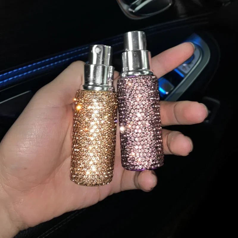 A hand holds two glass perfume atomizers, one gold and one pink, with silver spray tops.