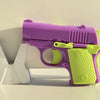 A purple and lime green mini 3D printed gravity fidget pistol toy resting on a white surface.