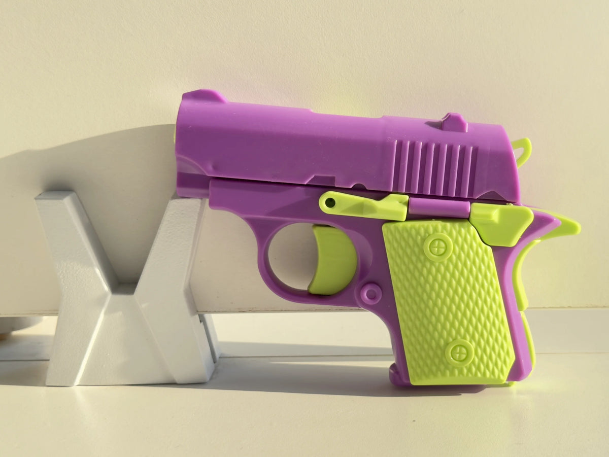 A purple and lime green mini 3D printed gravity fidget pistol toy resting on a white surface.