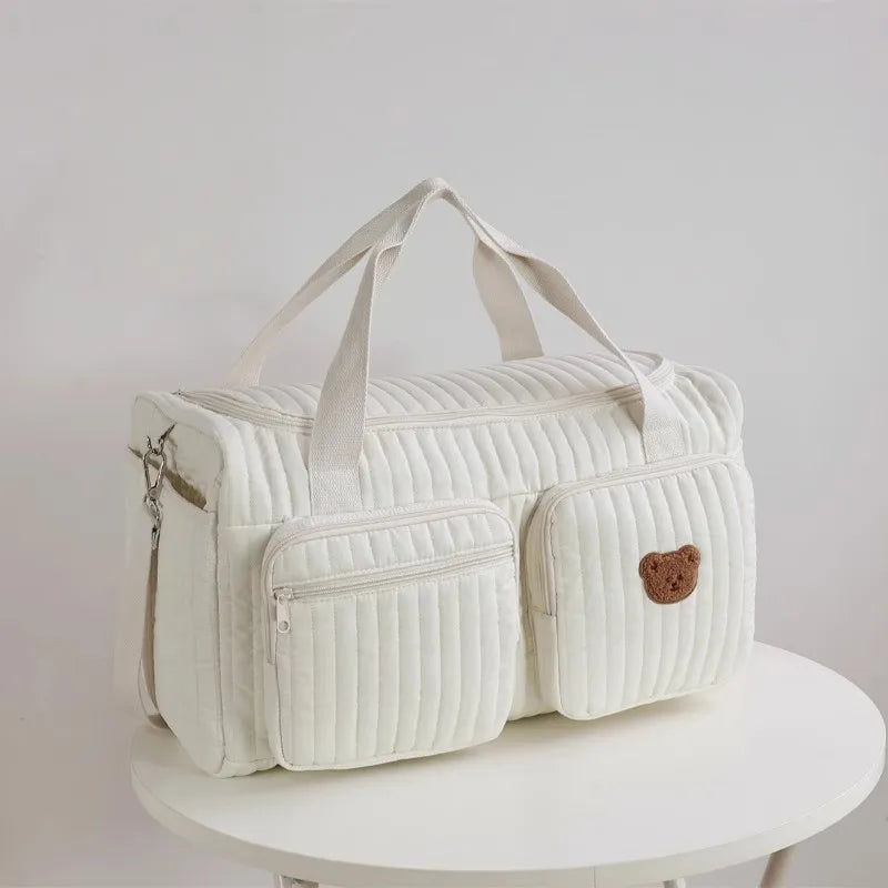 A cream-colored embroidered cotton diaper bag featuring a bear design.