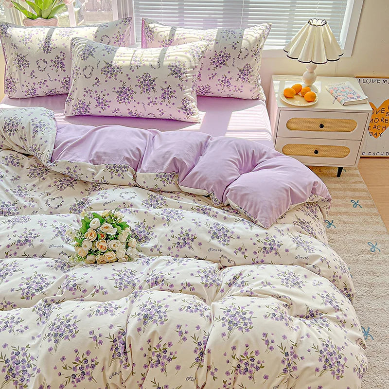 A lavender floral duvet cover set with matching pillowcases displayed on a bed next to a white nightstand.