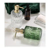 A green glass soap dispenser with a gold pump and a separate dark bottle are shown on a white marble surface.