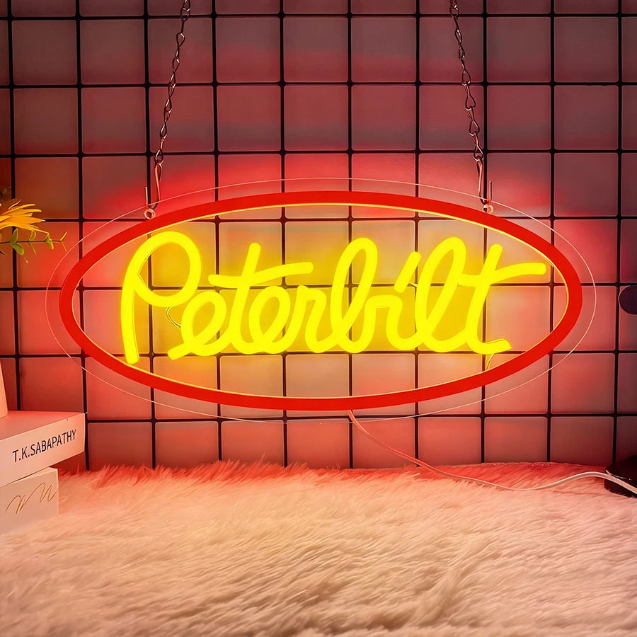 A bright yellow Peterbilt truck neon sign is displayed against a dark grid background, illuminated by red light.