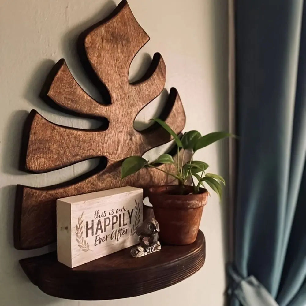 A rustic wooden wall-mounted storage rack featuring a leaf shape and a small potted plant.
