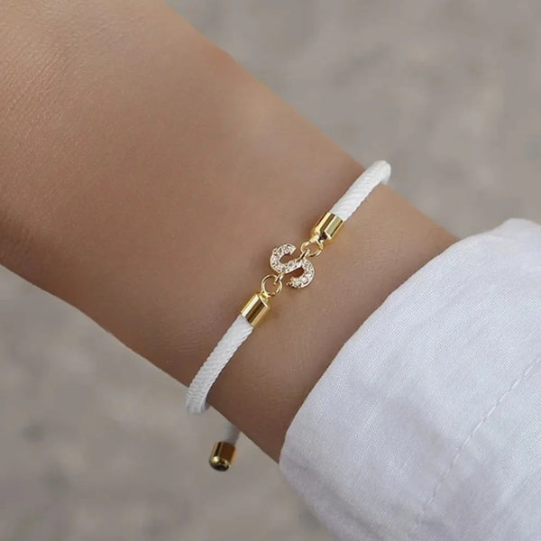 Nahaufnahme eines verstellbaren Anhängerarmbandes mit weißem Schnur und goldfarbenen Anhängern am Handgelenk.