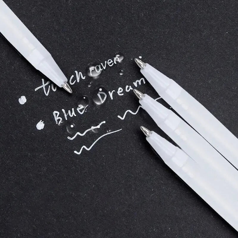 White ink pens are writing the words touch raven and blue dream on a black surface.
