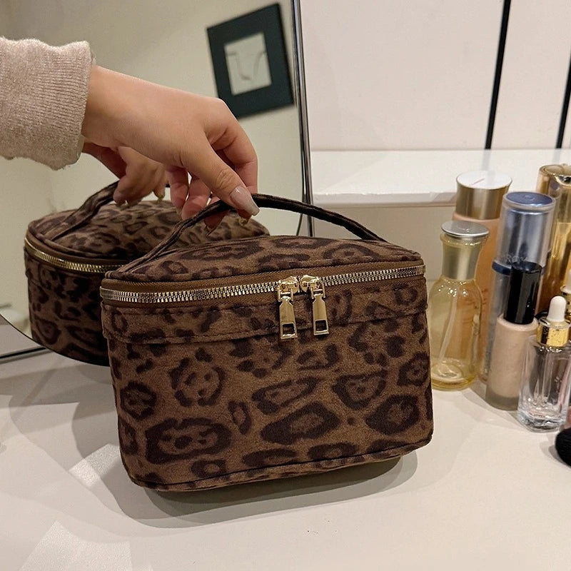 A brown leopard print cosmetic bag with a leather strap is displayed on a white surface.