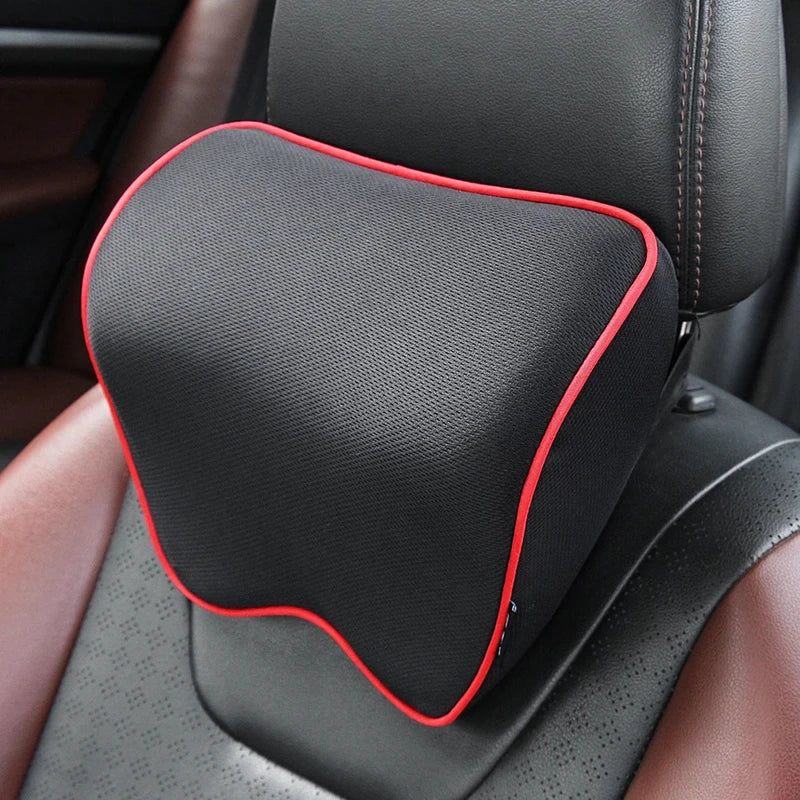 A black memory foam car headrest pillow with a red trim is shown in a vehicle seat.