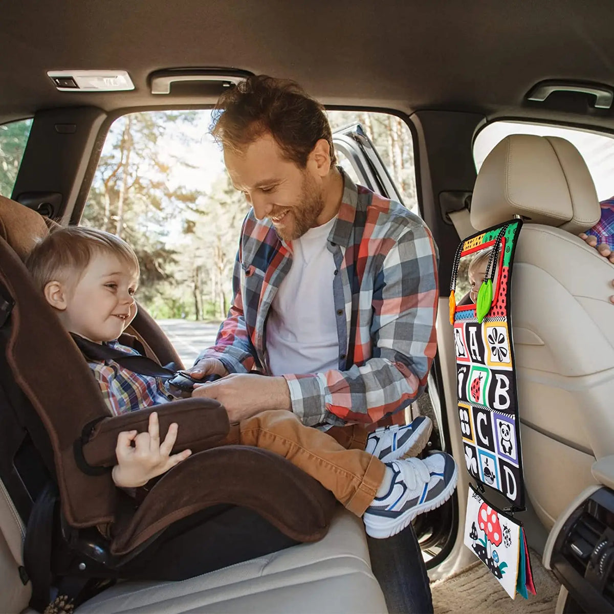 A father is reading a high-contrast crinkle cloth book with a tummy time mirror to his baby in the car.