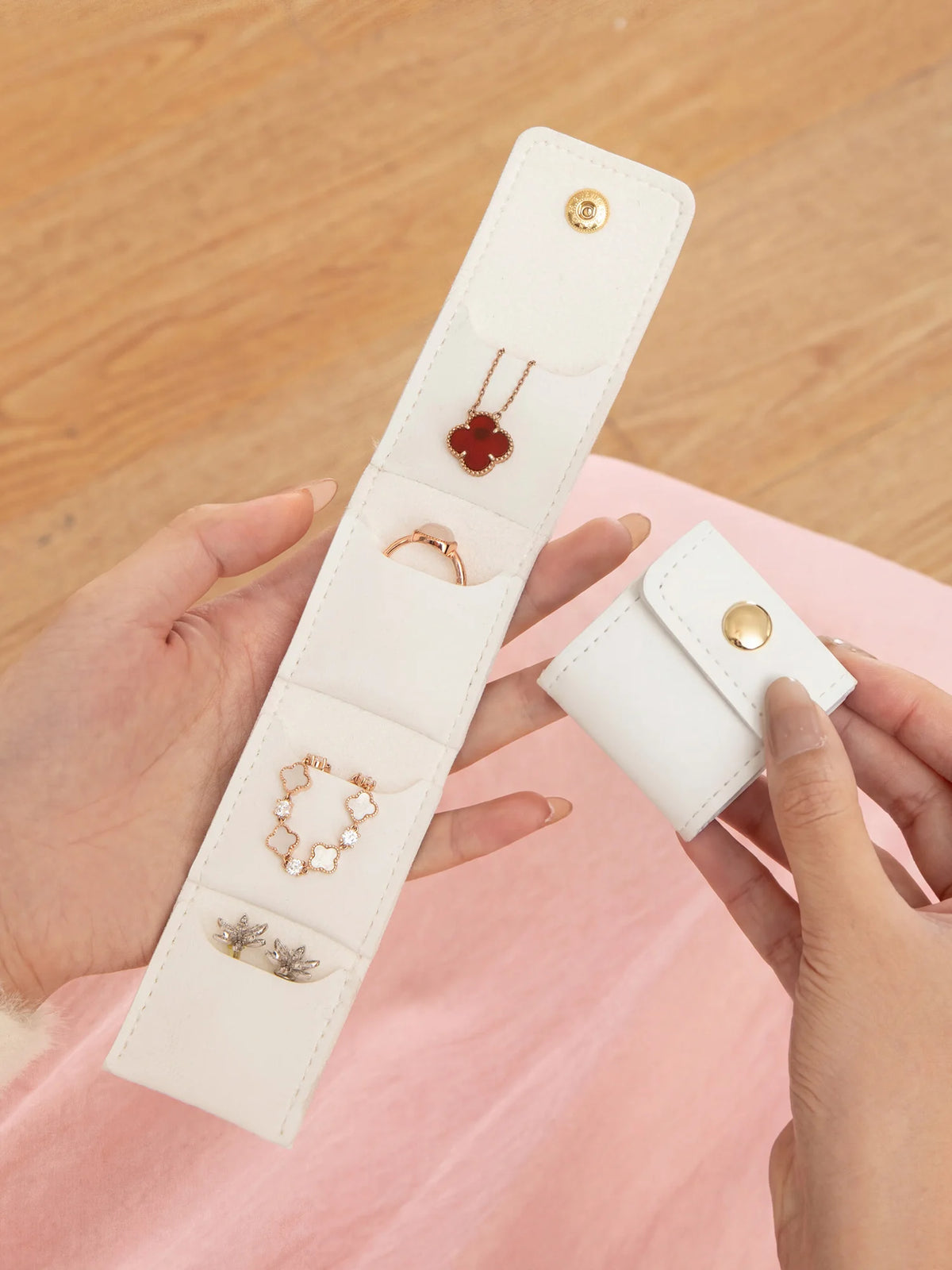 A hand holds a white PU leather jewelry organizer pouch with four compartments, displaying various rings and earrings.