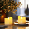 A glowing yellow LED tea light candle sits on a silver plate on a wooden surface.
