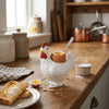 A white ceramic chicken egg cup holding a raw egg, placed on a wooden table with bread slices.