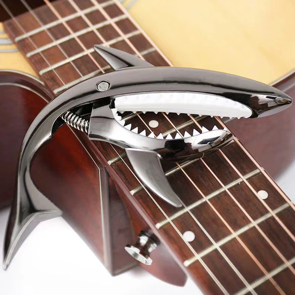 A close-up of a pro-grade zinc alloy guitar capo with a silver body and black teeth, resting on a wooden fretboard.