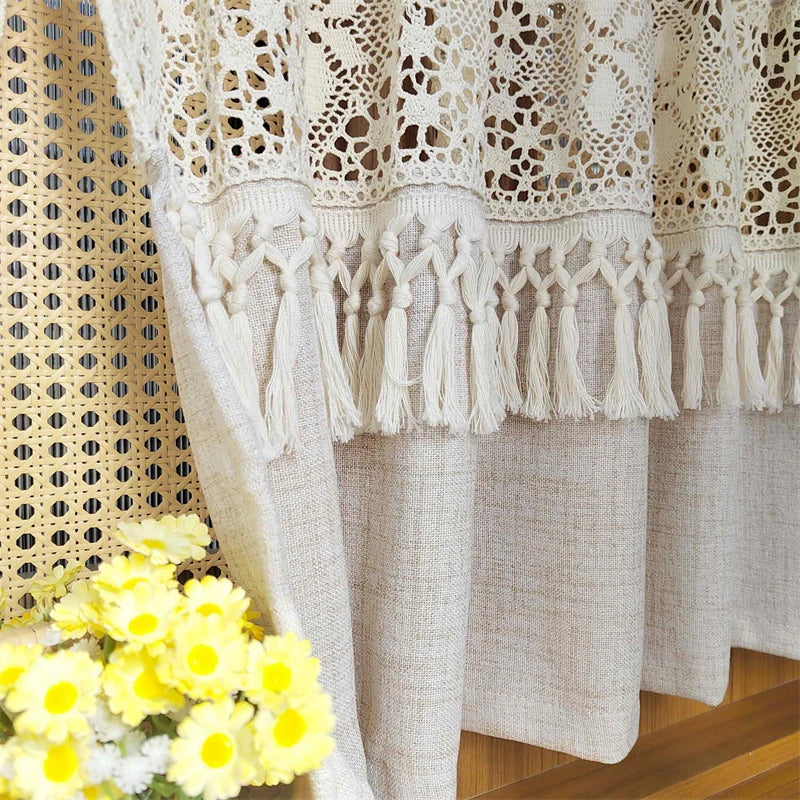 Beige sheer curtain with lace trim and tassel fringe hanging in a light-colored fabric drape.